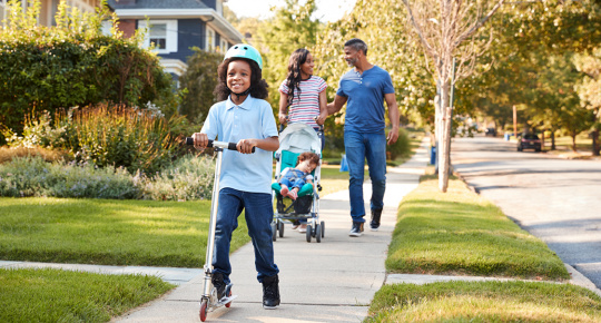 Young family with children enjoying a walk together down a quaint neighborhood sidewalk.