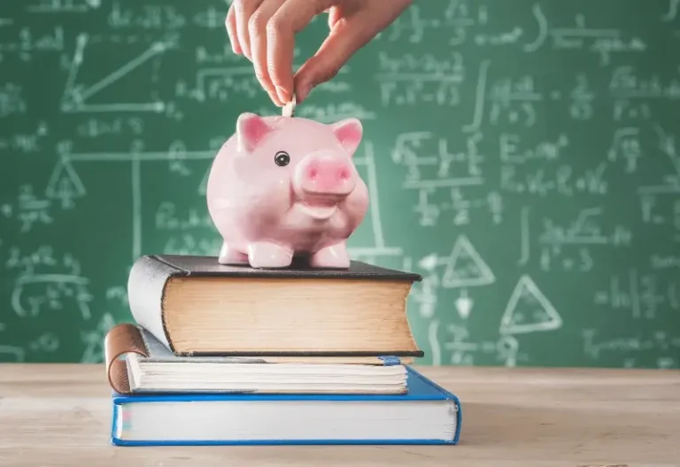 Female putting coins into a piggy bank that is sitting on top of school books.